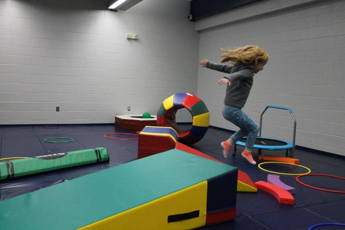 child jumping off of large gymnastics wedge in a room full of tumbling equiptment