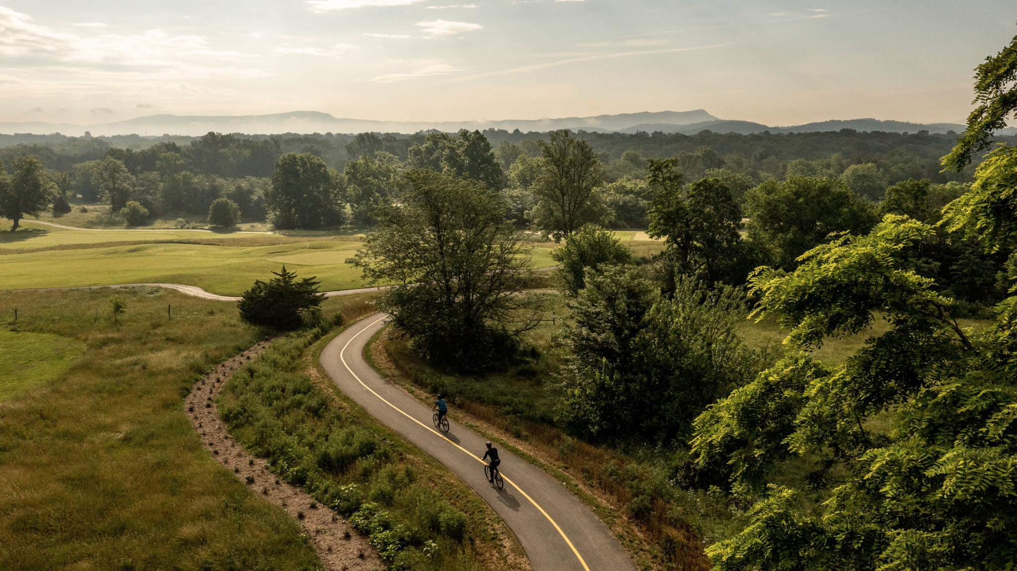 Two bicyclists on a trail with mountains in the background