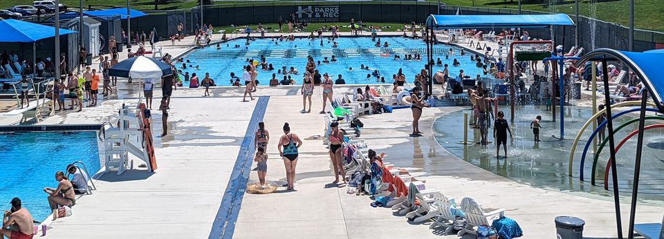 Busy day at the outdoor pool with people walking and swimming